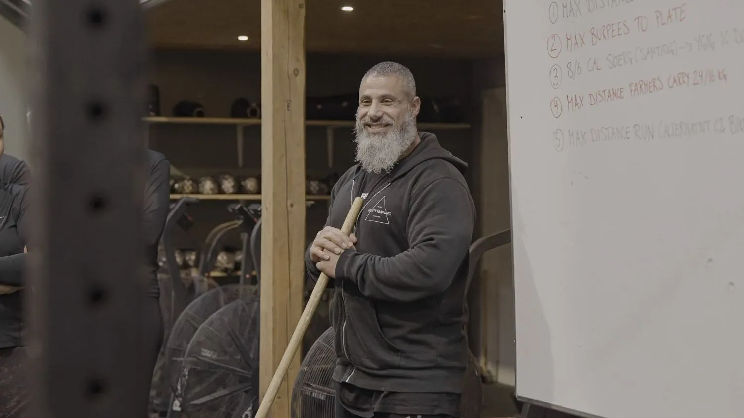 Smilende coach med træningsstav ved tavlen med dagens træningspas