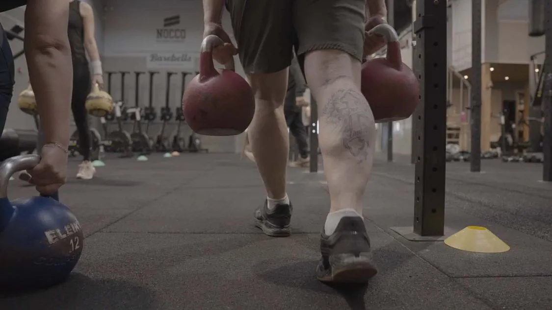 Medlem laver farmers carry med to kettlebells hen over gulvet i træningssalen